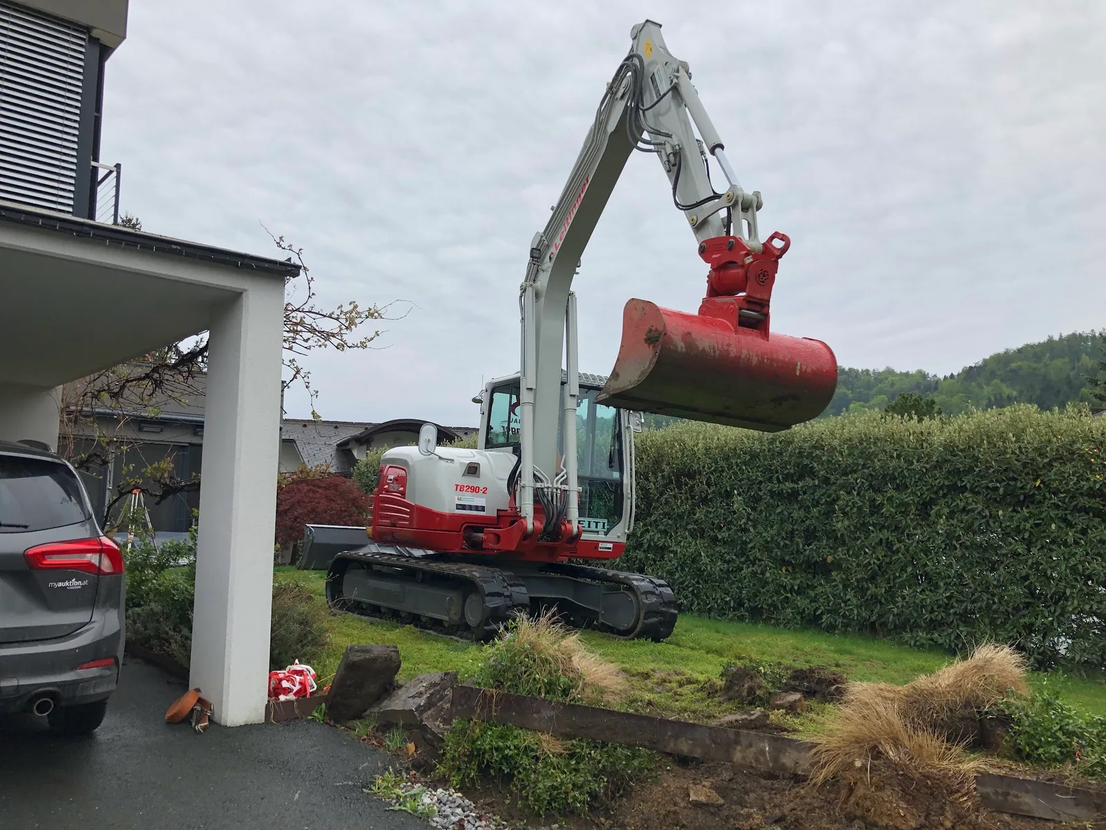 Bagger bei Erdarbeiten in einem Garten neben einem Carport