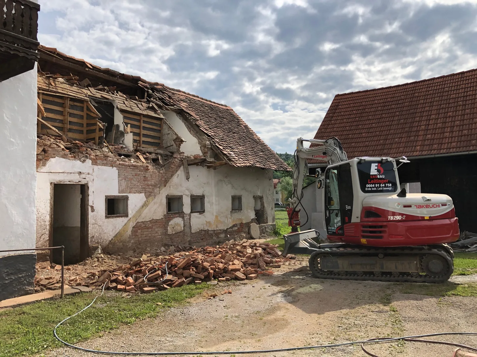 Bagger vor einem teilweise abgebrochenen Gebäude und Ziegelhaufen